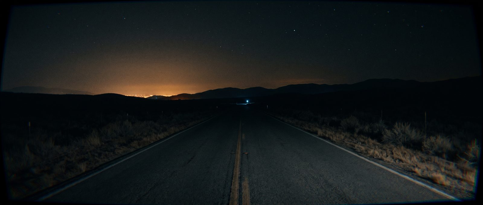 Night road: An empty two-lane under a distant city glow.