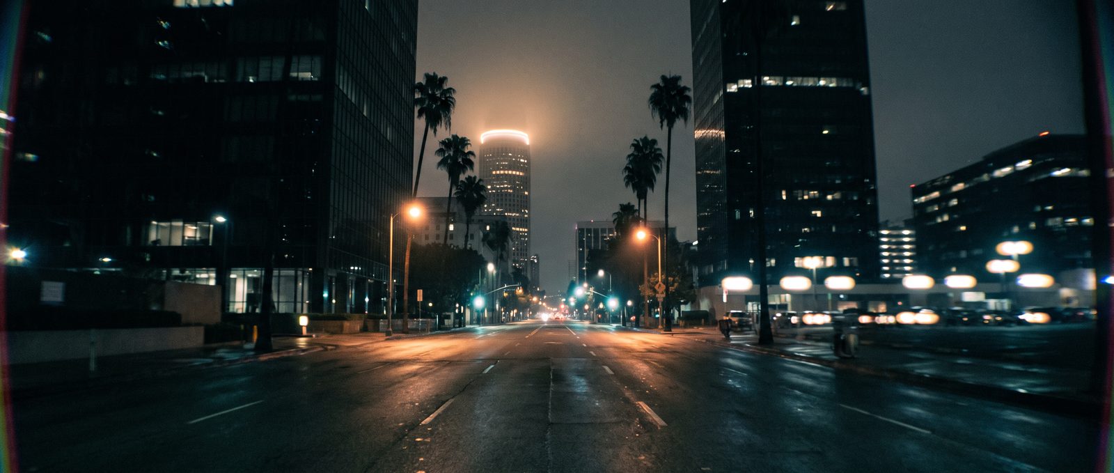Downtown: An empty downtown canyon at night: wet asphalt between dark towers.